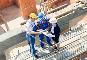 Motiv: Drei Menschen stehen auf einer Baustelle und sehen sich einen Plan an (Foto: Kzenon - Fotolia.com)