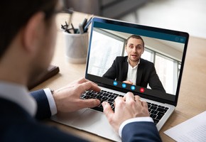 Motiv: Ein Mann schaut auf einen Laptop, auf dem ein anderer Mann in einer Videokonferenz zugeschaltet ist. (Foto: fizkes - stock.adobe.com)