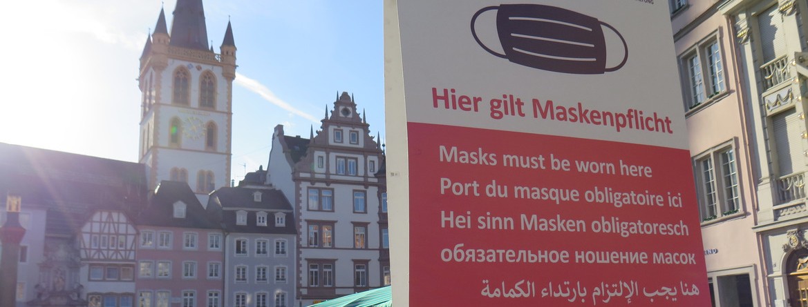 Motiv: Auf dem Hauptmarkt der Stadt Trier weist ein Schild auf die dort geltende Maskenpflicht hin.